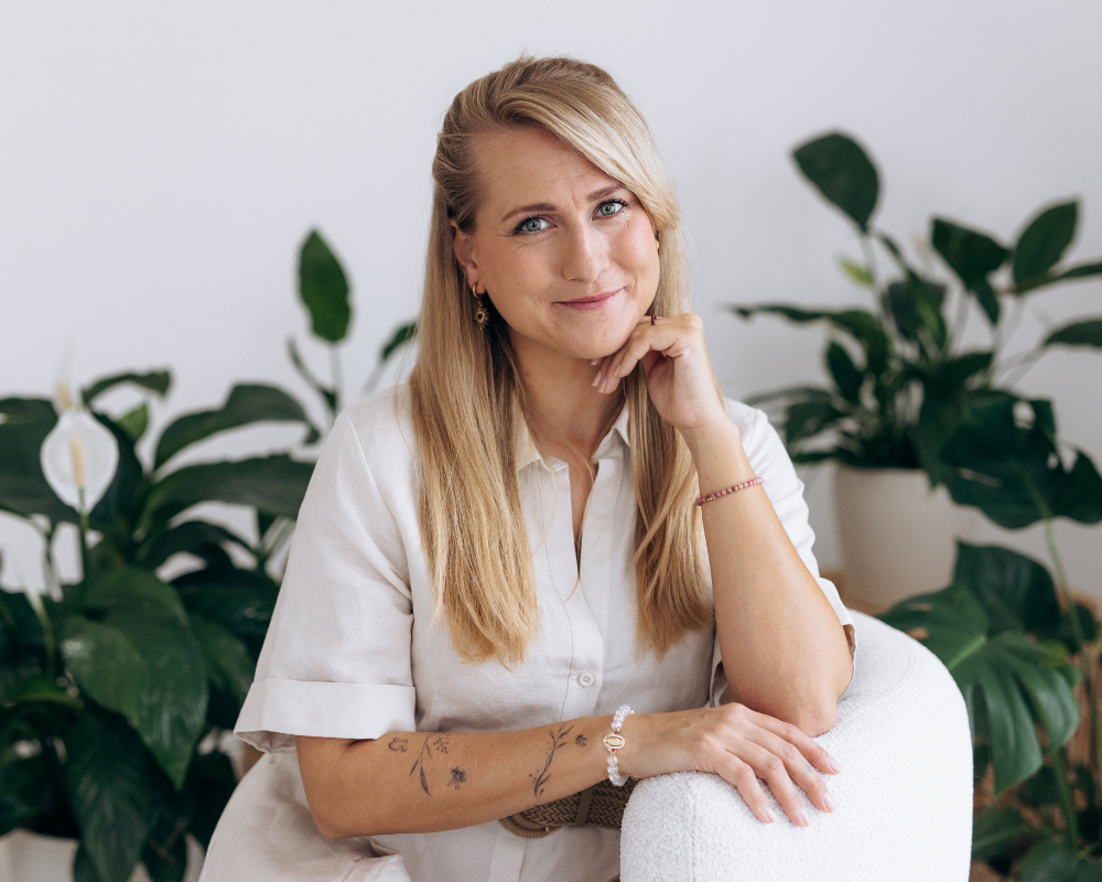 Kristy Stehnová z projektu RestartujSe s Kristy sedí v klidném prostoru s rostlinami, opírá se o křeslo a jemně se usmívá.